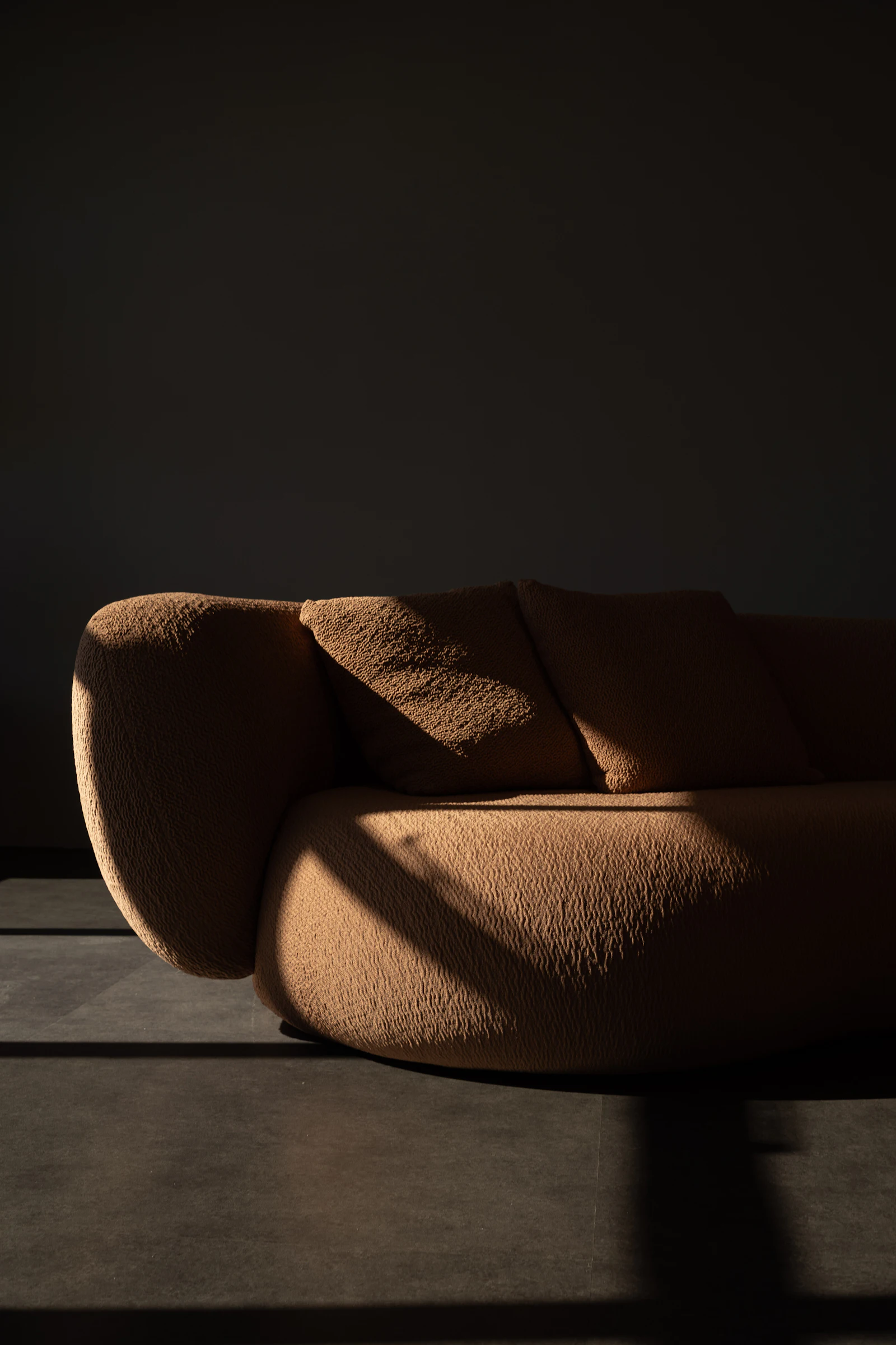 A textured brown sofa caught in a slanting beam of sunlight