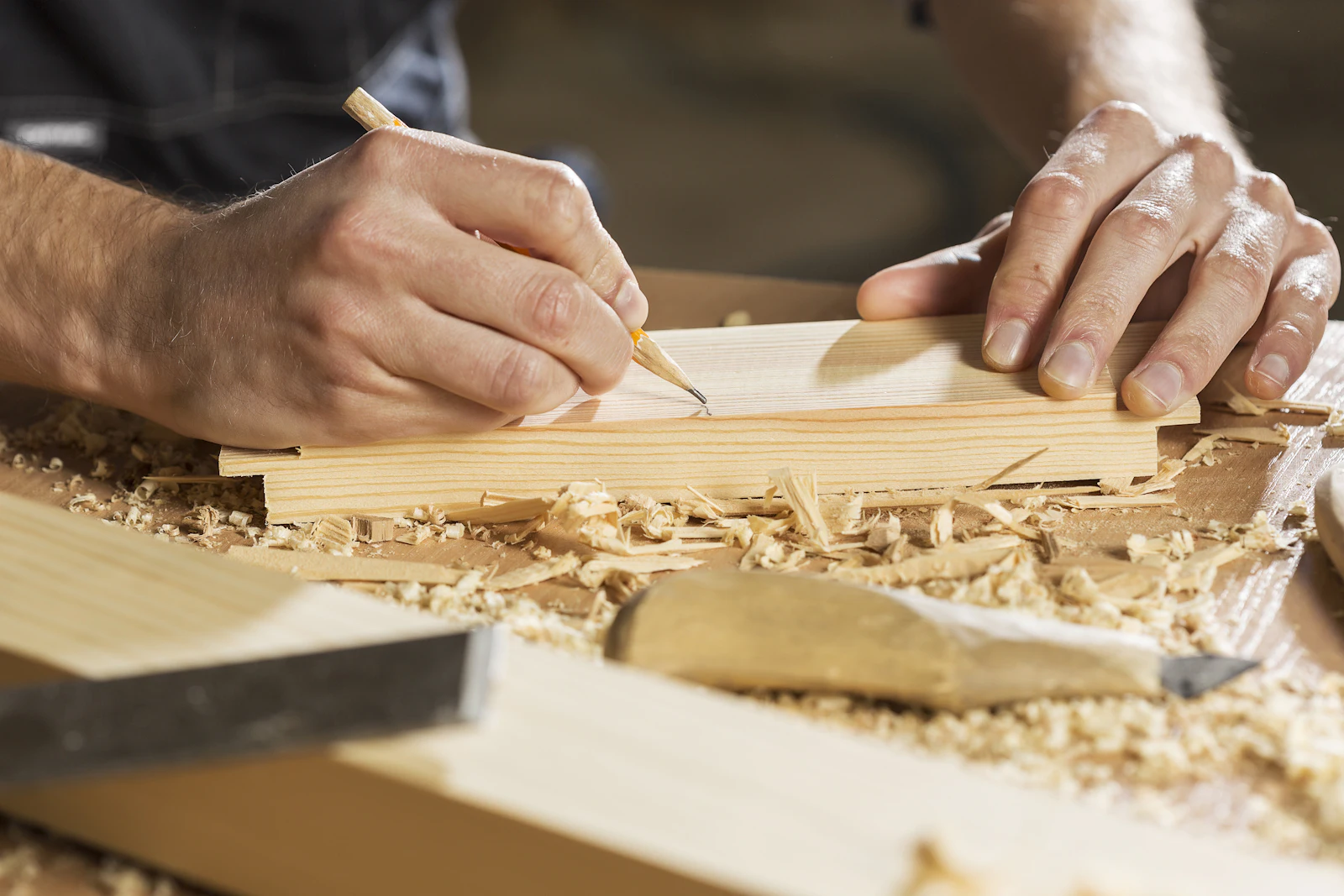 Hands marking a wooden board with a pencil in a workshop full of shavings