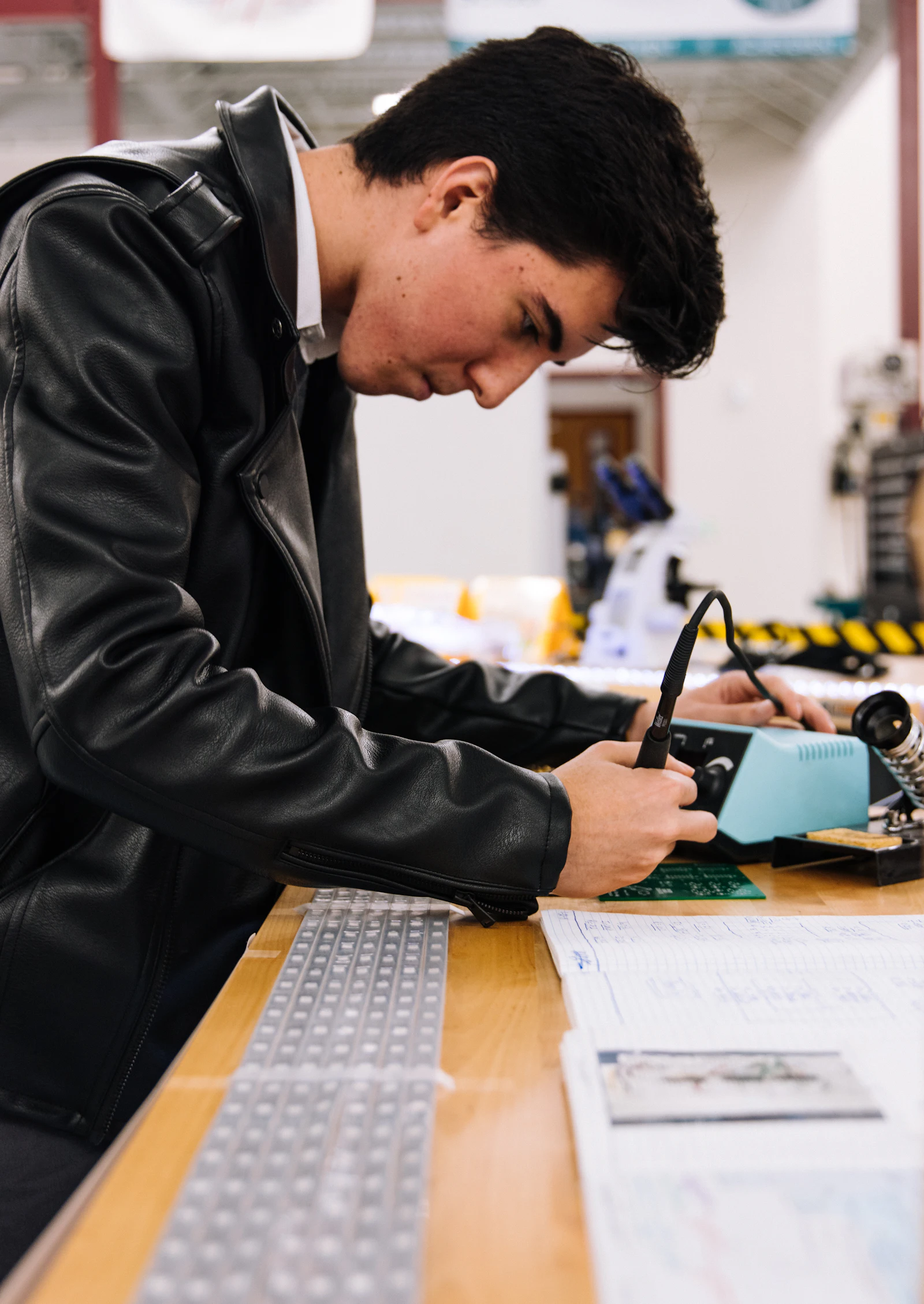 A student soldering a circuit board at a workbench in an engineering workshop