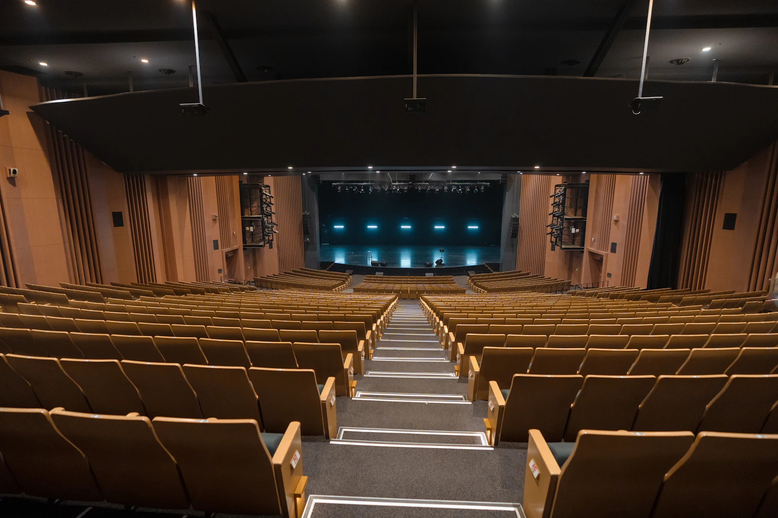 An empty auditorium with rows of wooden seats facing a lit stage