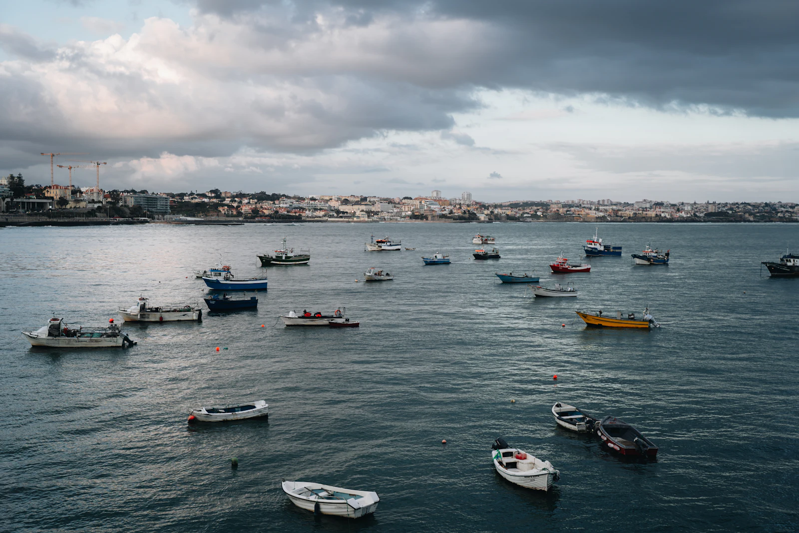Small boats anchored in a grey bay with a coastal town behind