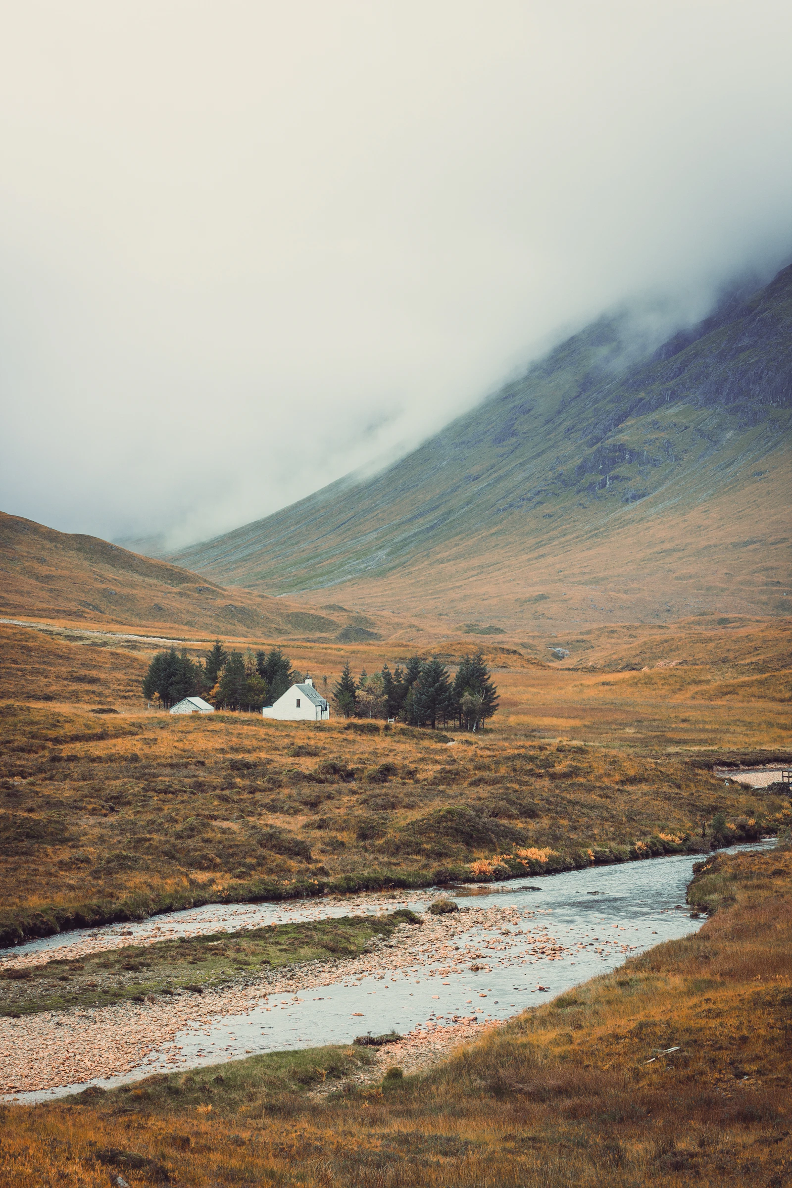 A stream winding through a green valley with misty hills and white cottages