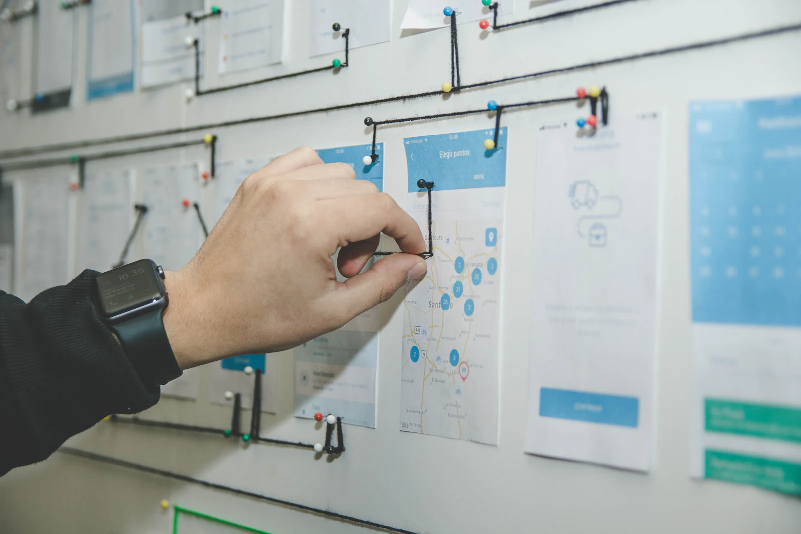 A hand arranging printed screens and notes on a planning board