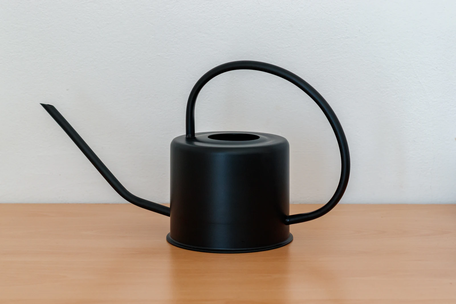 A black watering can with a long, thin spout on a wooden table